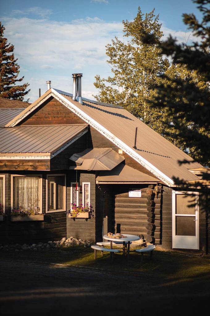 Evening sun on a log building at Eagle's Nest Resort, with a picnic
                      table, flower boxes and a screen door.