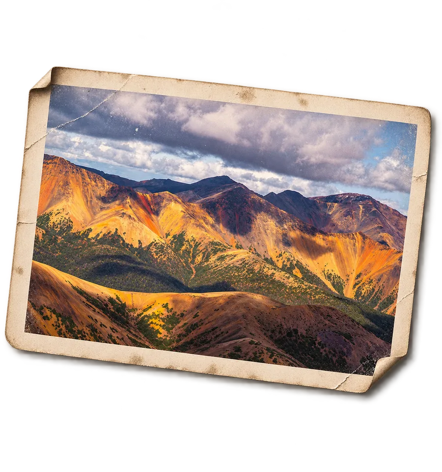 The Rainbow Range at evening, its volcanic
               slopes streaked orange, gold and rust, as a weathered print.
