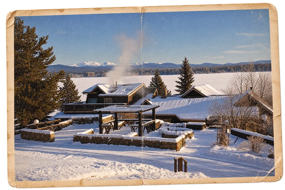 The lodge and its stone garden walls under deep
             snow, smoke rising from the chimney and the frozen lake running to the far shore
             beyond, as a weathered print.